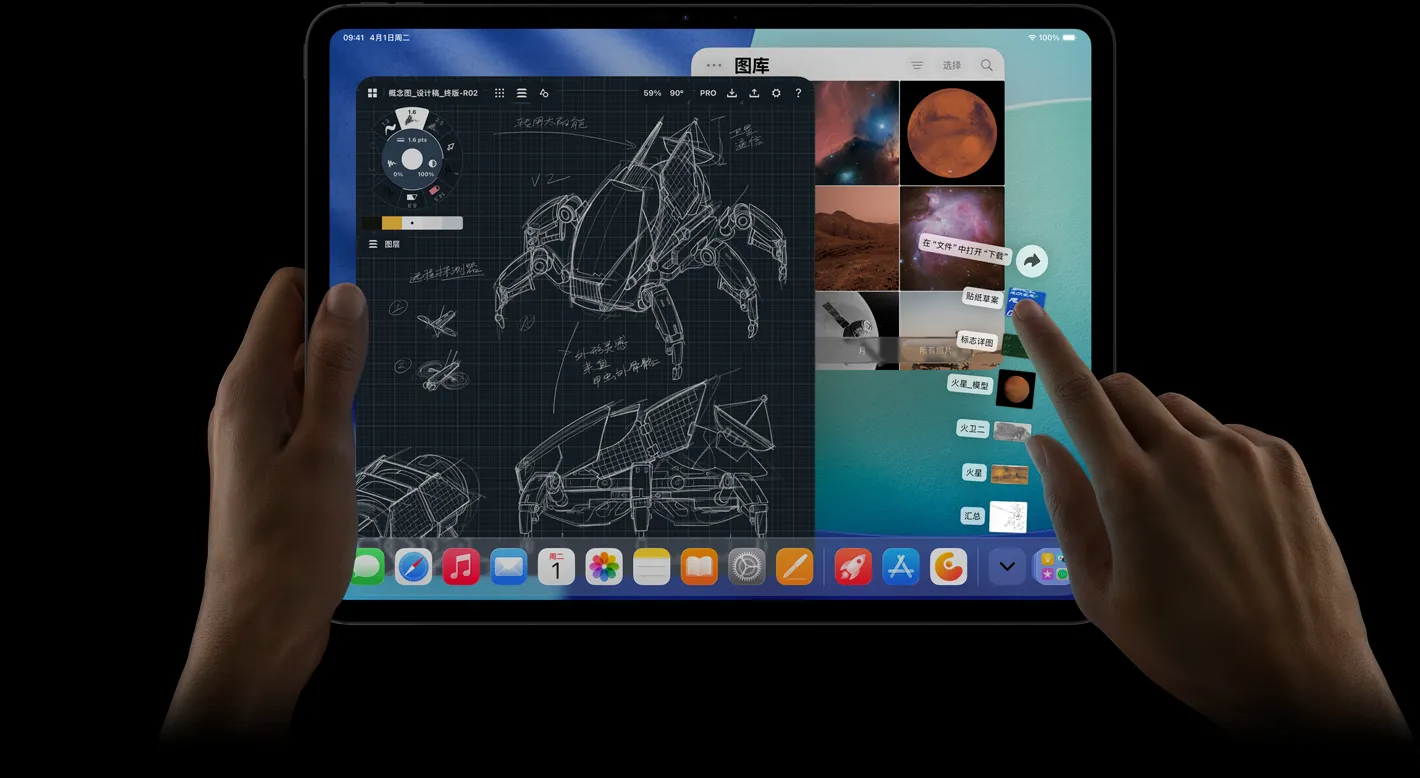 横屏放置的 iPad Pro 正面外观，右手指向屏幕中呈扇状展开的“下载”文件夹文件。屏幕上的 iPadOS 26 界面展示多款打开的 app，其中包括带有详细机器人插图、手写注释及多个设计阶段的照片编辑 app，以及照片图库。