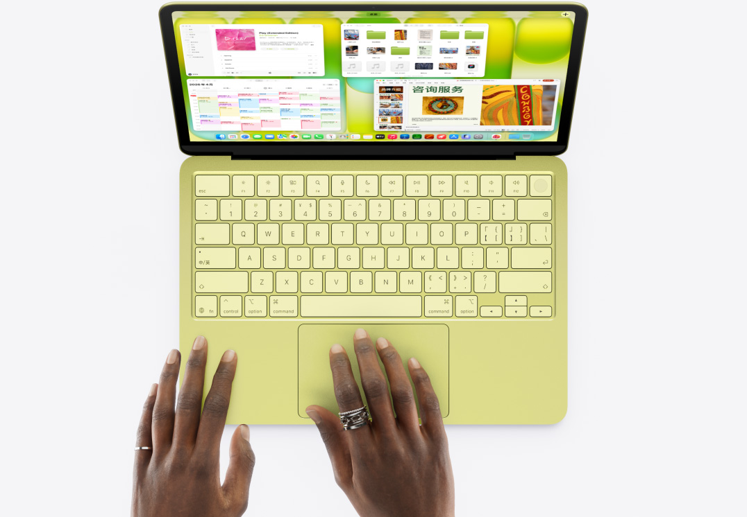 柑橘黄色 MacBook Neo，用户的一只手放在触控板上，屏幕显示多个打开的窗口，其中包括音乐和日历 app。