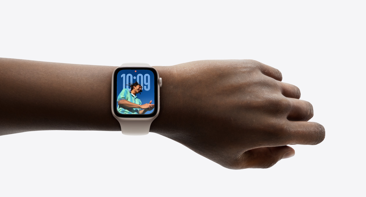 特写画面显示一只手腕戴着配有橡胶表带的玫瑰金色 Apple Watch，表盘展示全新 Liquid Glass 设计的时间数字。