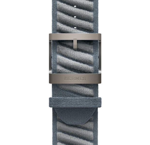 Apple Watch Hermès Ultra 3 En Mer 表带，展示 Bleu Gris/Bleu Glacier 灰蓝配冰川蓝色 (蓝灰色配浅灰色斜条纹) 配色、针织聚酰胺纱线材质、位于表带中央的调节孔，以及镌刻有 Hermès 爱马仕标志的原色钛金属表扣。