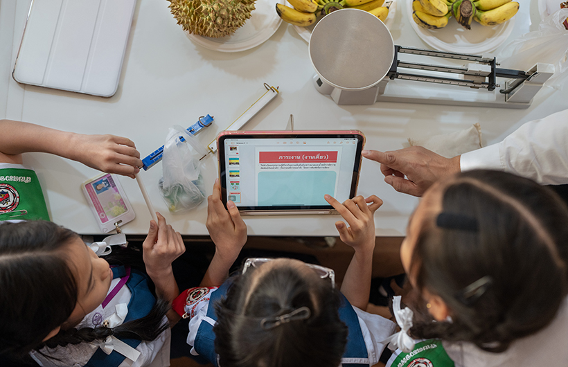 三名小学生围在 iPad 旁，协作完成一份科学项目的演示文稿。