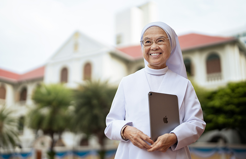 校长 Sister Françoise Jiranonda 手持 iPad 站在学校门外。