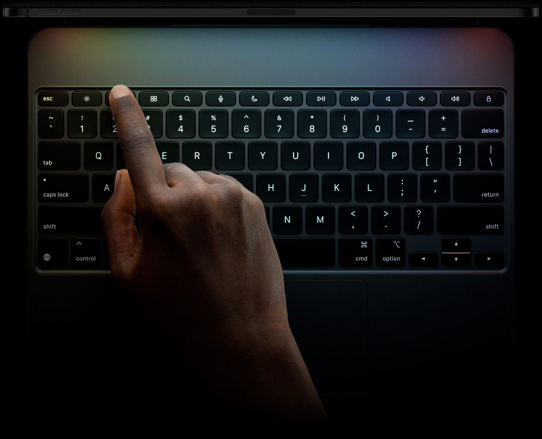 横屏放置的深空黑色 iPad Pro 与横向放置的妙控键盘相连。iPad 展示顶部边缘轮廓。键盘展示正面外观，包括黑色背光按键、整排功能键、Esc 键、Tab 键、大写锁定键、左侧 Shift 键、Control 键、Option 键、右侧 Shift 键、Delete 键、Return 键、呈倒 T 形排列的方向键和内置触控板。
