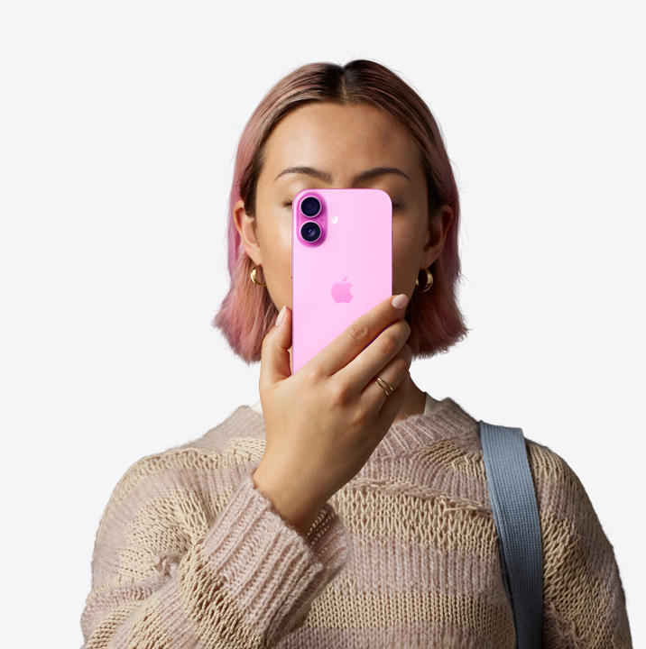 一个人将粉色 iPhone 16 至于面部前方，展示背面外观和机身左上角的双摄系统。
