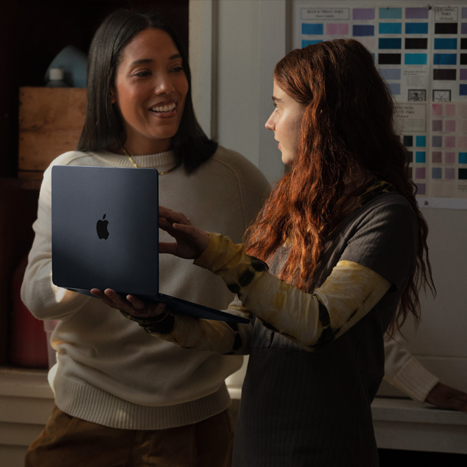 一名教师和一名学生正在交谈，手里拿着一台 MacBook 笔记本电脑