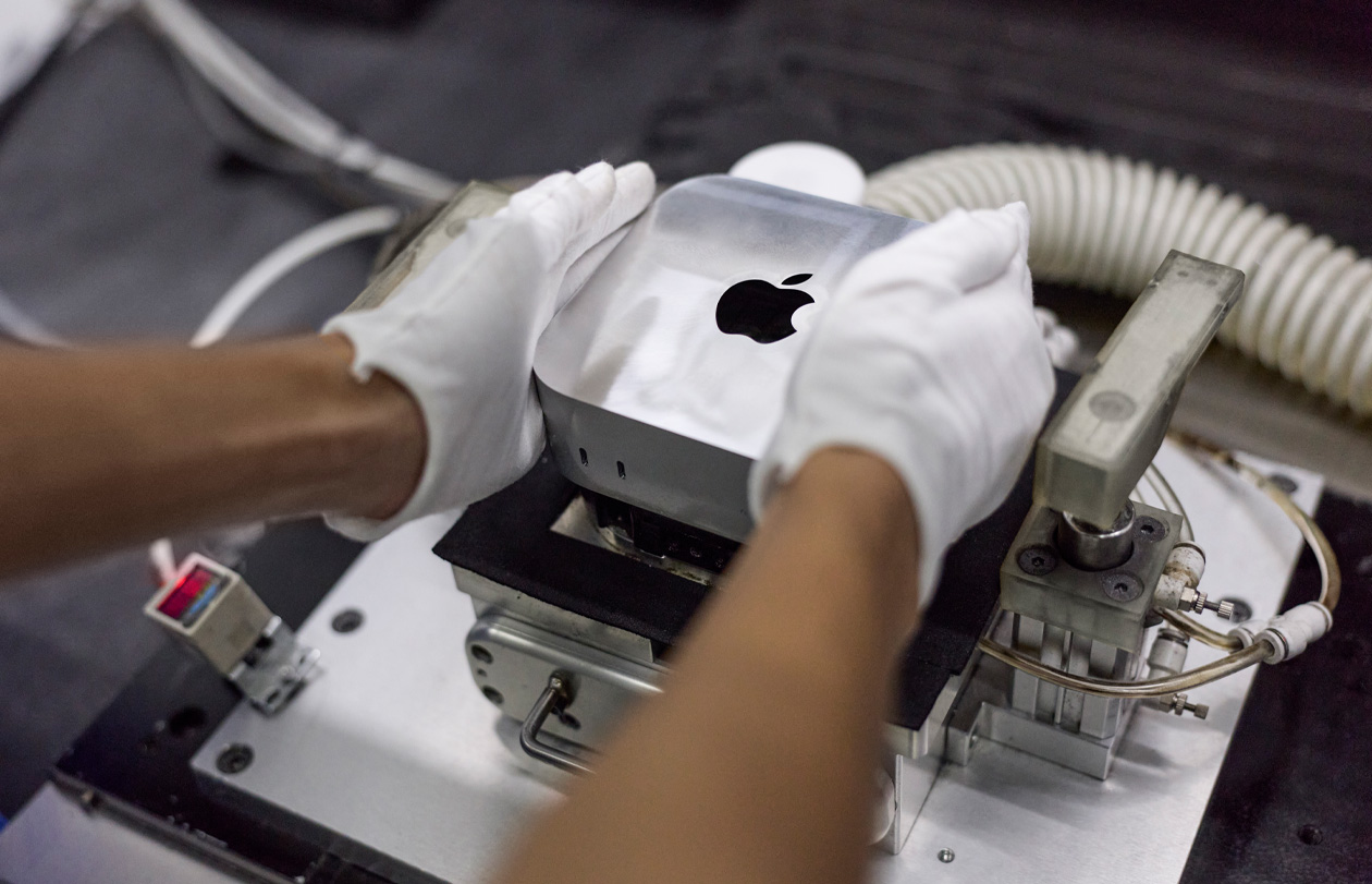 戴着手套的双手在组装期间将 Mac mini 放入制造机中