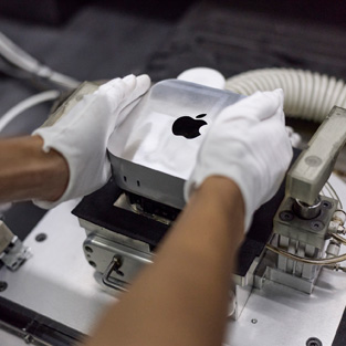 戴着手套的双手在组装期间将 Mac mini 放入制造机中