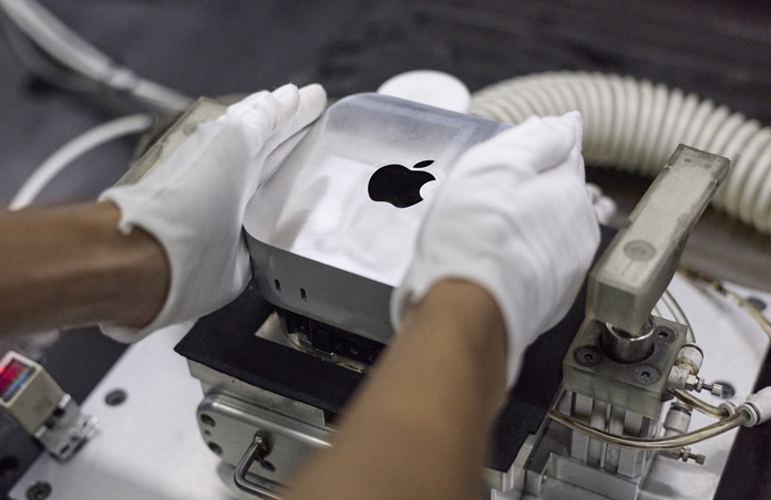 戴着手套的双手在组装期间将 Mac mini 放入制造机中