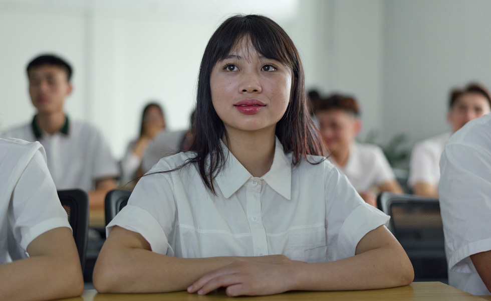 六位身着白色短袖衬衫的人坐在教室里，神情专注地看着前方