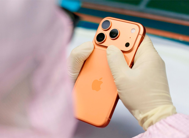 一名身着全罩式工作服的员工在工作台前检查 iPhone